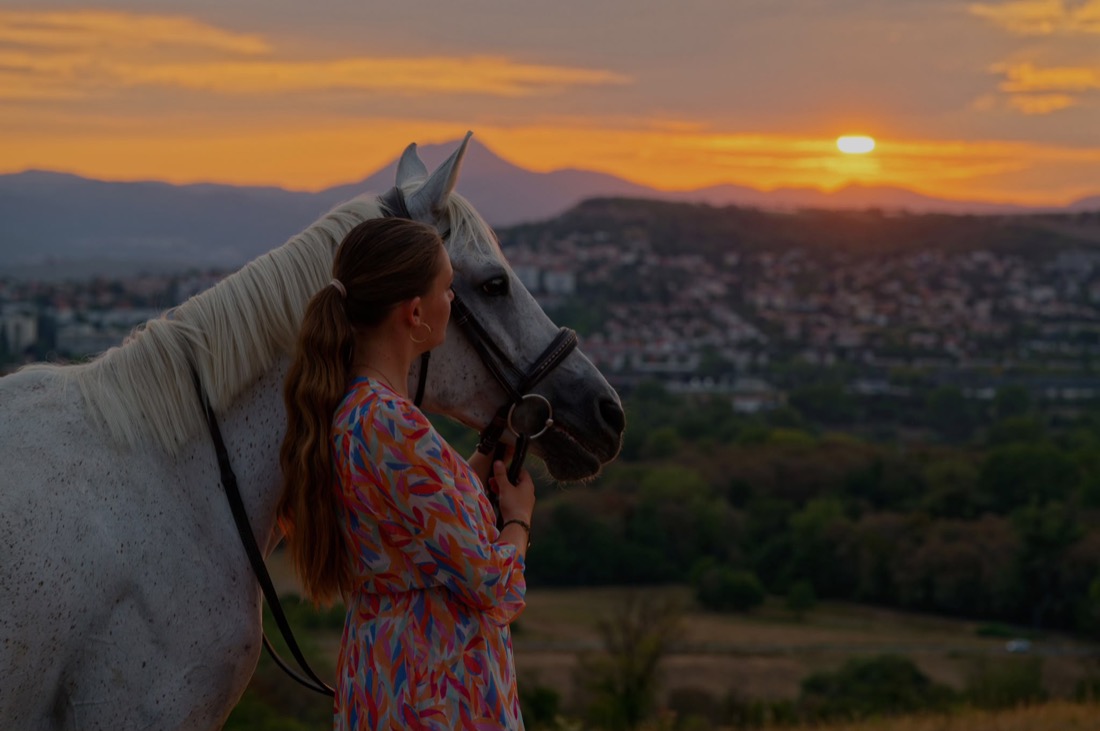 Emma beside her grey mare at sunset